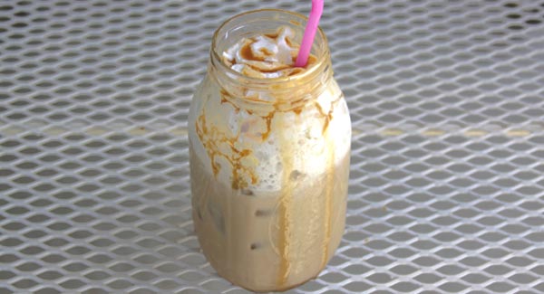 Tall Glass Filled with Ice Cubes and Vanilla Coffee with Whip Cream and Caramel Sauce.