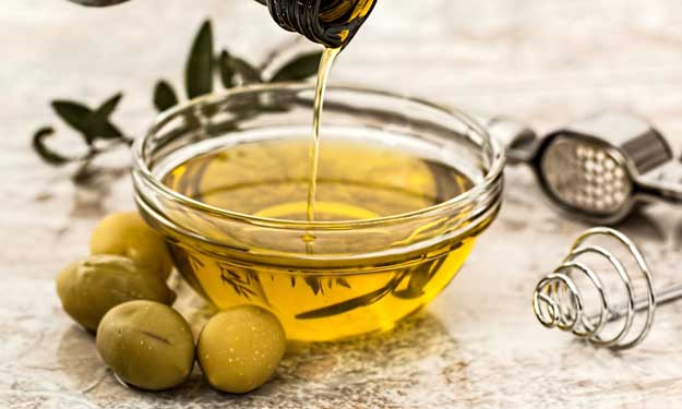 Olive oil pouring into a glass bowl with fresh olives, representing plant-derived squalane oil.